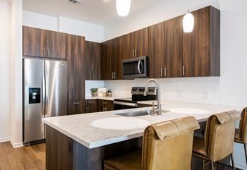 A modern kitchen with a stainless steel refrigerator, microwave, and a marble countertop.